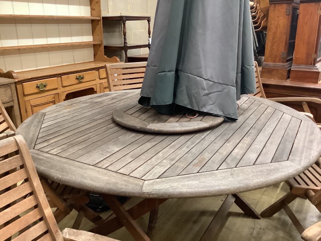 A circular teak garden table, 150cm diameter, height 74cm eight teak folding chairs, parasol and base (parasol rope is broken)